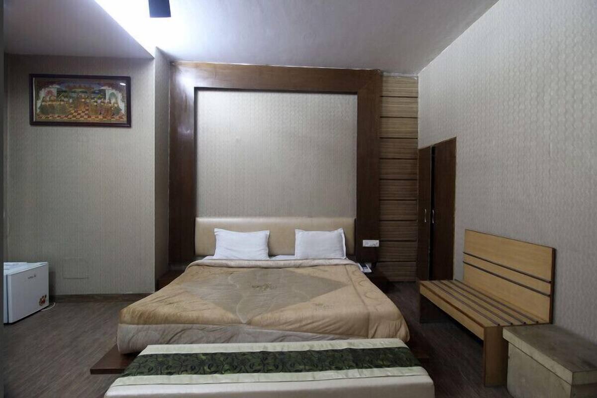 Habitación de hotel con una cama grande, un banco, una mesita y un cuadro en la pared.