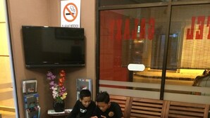Two people sitting at a wooden table with a red top, in a room with a no-smoking sign and a television mounted on the wall. - Galaxy Inn (Lumut)