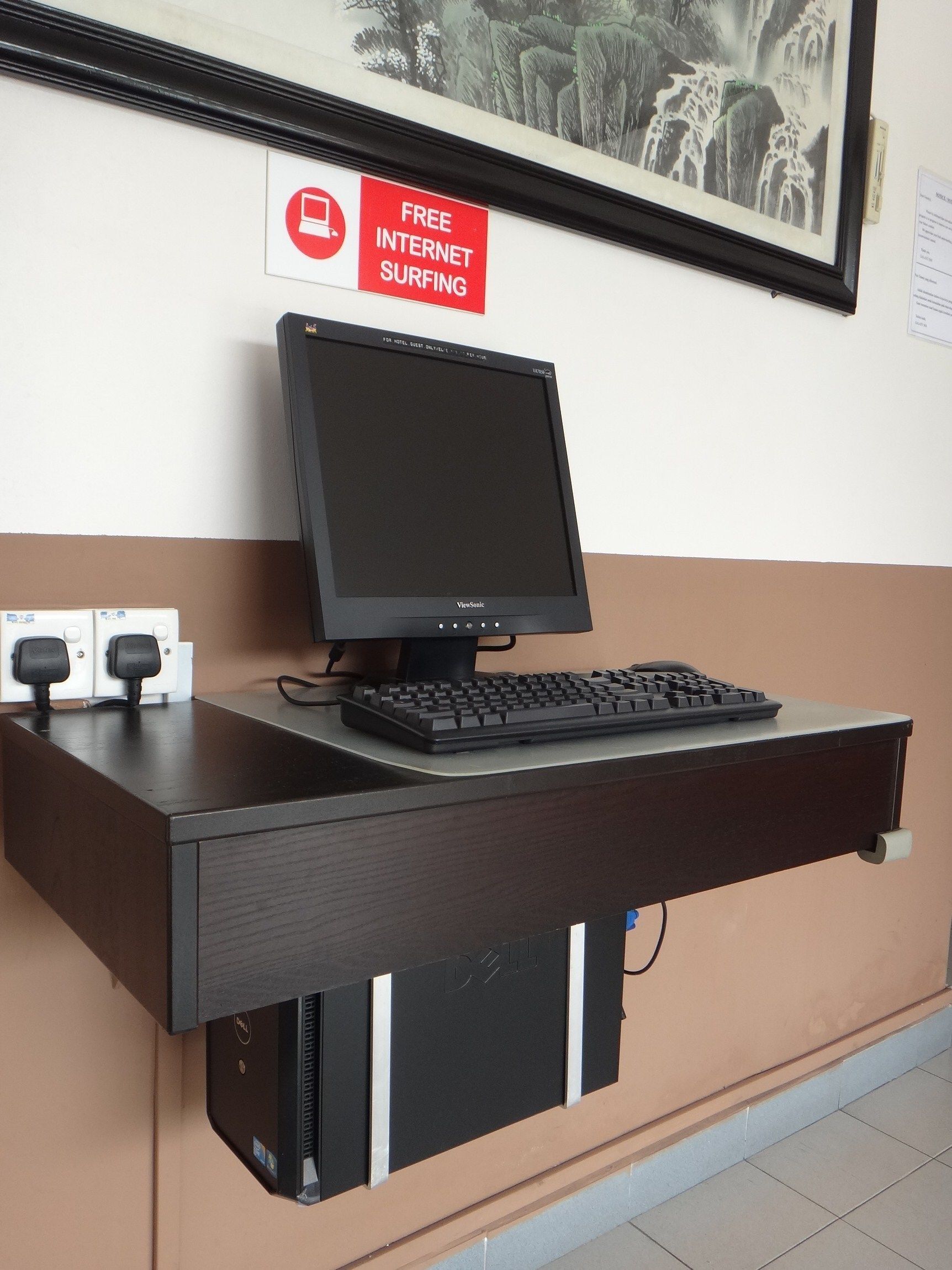 Un bureau équipé d’un écran ViewSonic, d’un clavier et d’une souris, une affiche indiquant un accès gratuit à Internet et un tableau encadré accroché au mur.