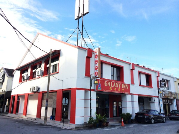 A Galaxy Inn building with a red and white facade, air conditioning units, and a parking area with cars.
