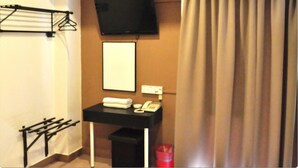 A hotel room with a black desk, a TV mounted on the wall, a towel rack, a small trash bin, and a curtain. - Galaxy Inn (Lumut)