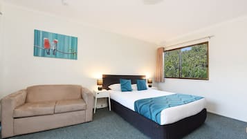 Habitación de hotel con cama, sofá, mesita de noche, lámpara y ventana con cortinas.