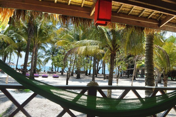 A beach scene with a hammock, palm trees, and a thatched roof structure.