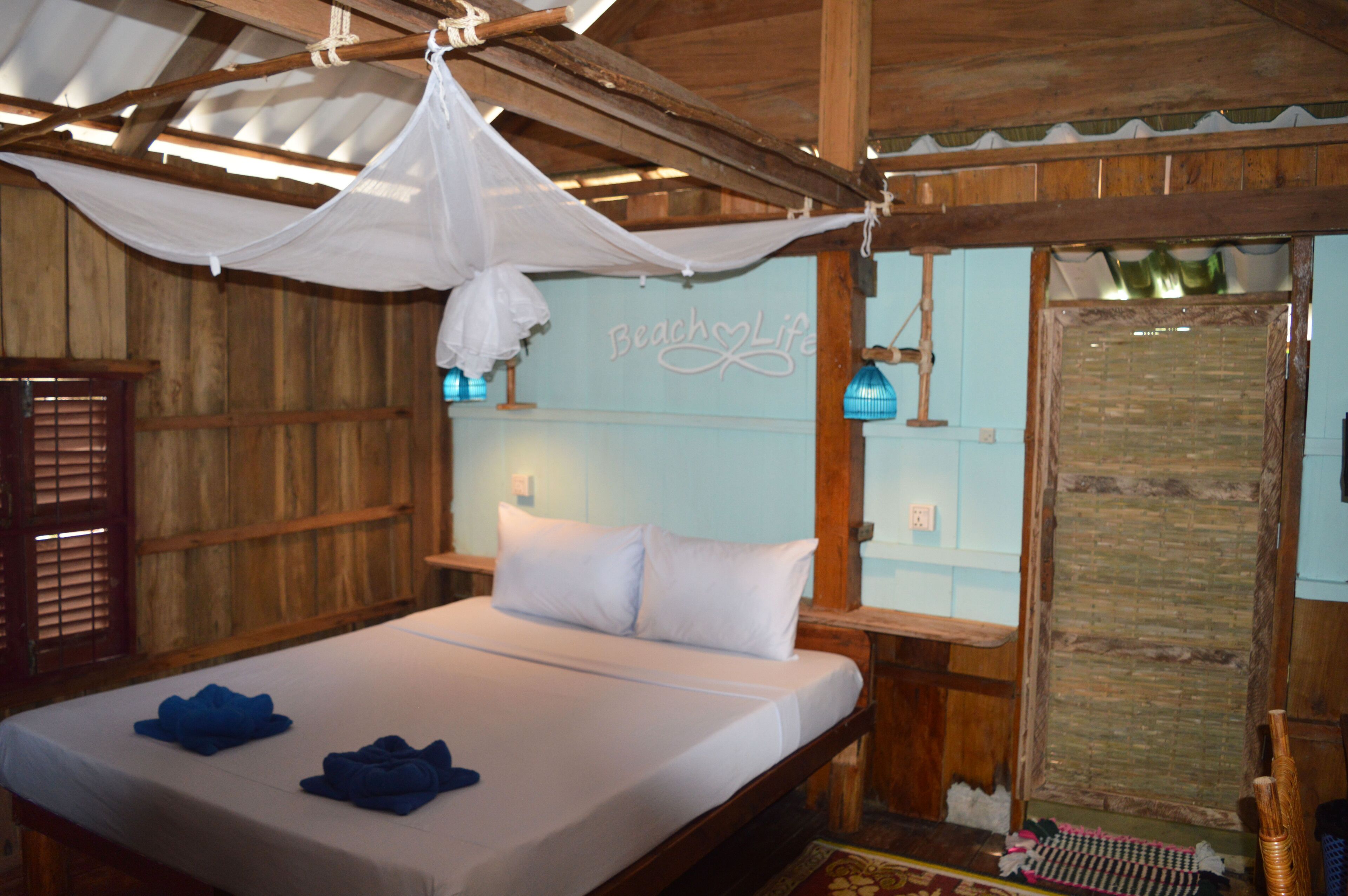 A room with a bed, wooden walls, a mosquito net, and a sign reading "Beach Life".