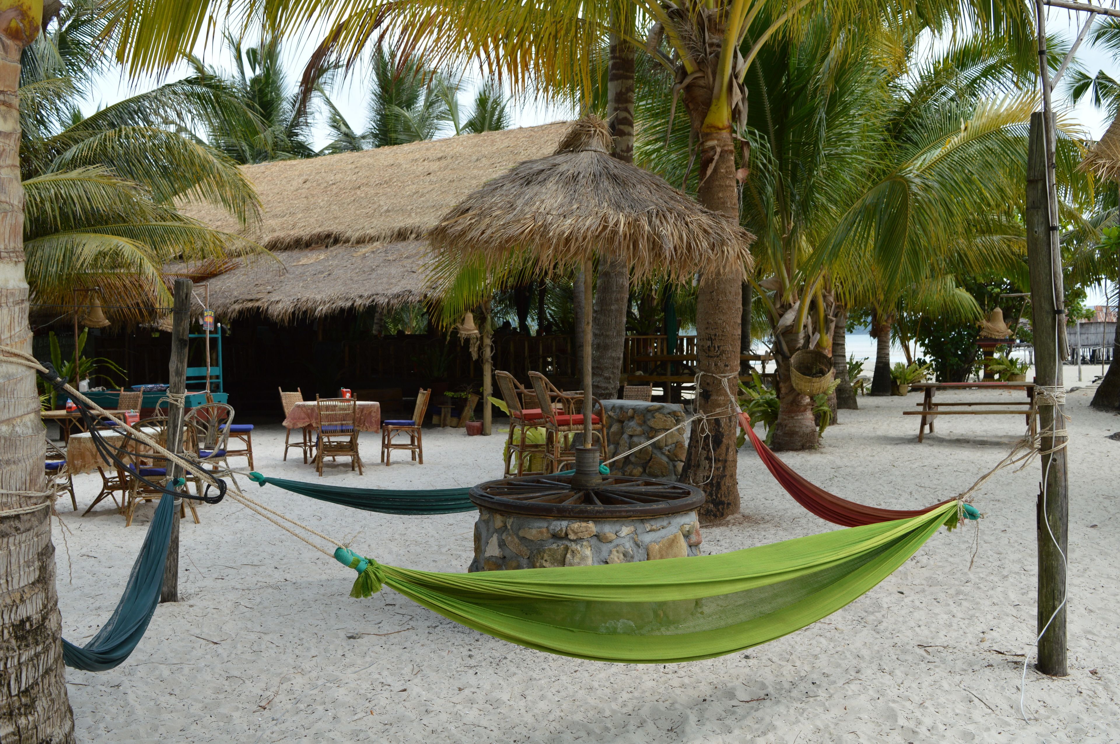 A beach setting with a thatched-roof hut, wooden furniture, and a hammock.