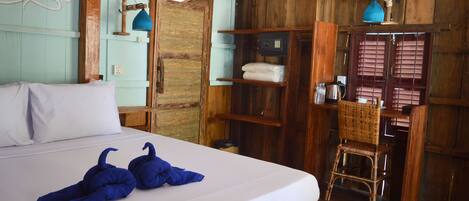 A wooden room with a bed, a chair, and a shelf with towels.