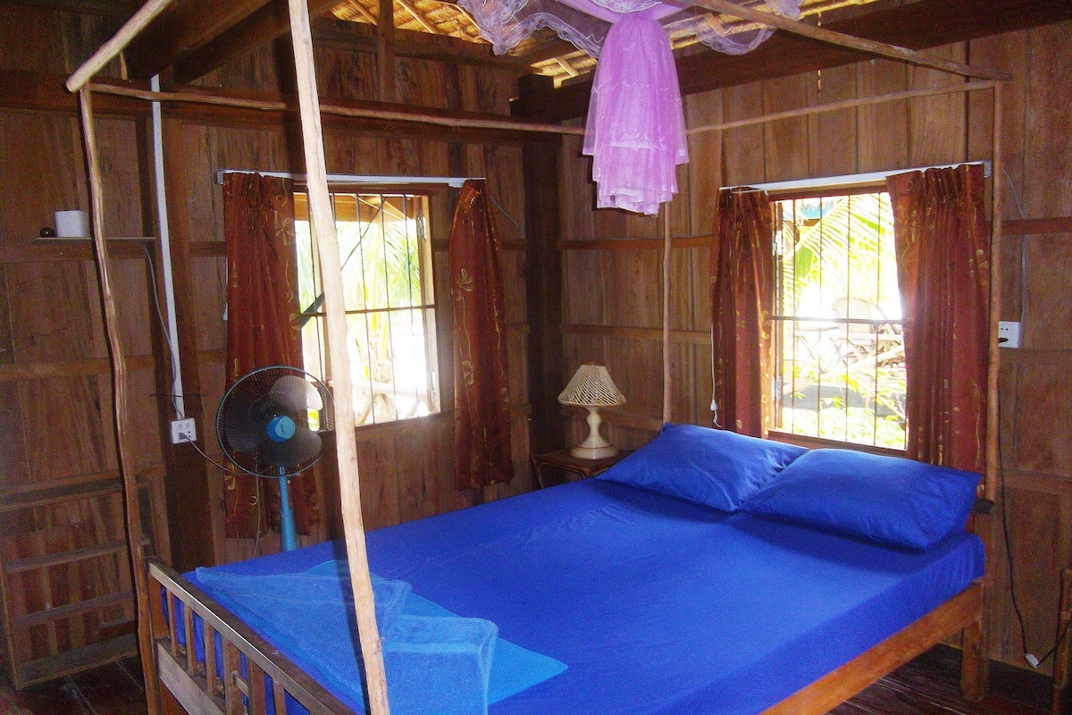 Une pièce en bois avec un lit, un ventilateur et une fenêtre avec des rideaux.