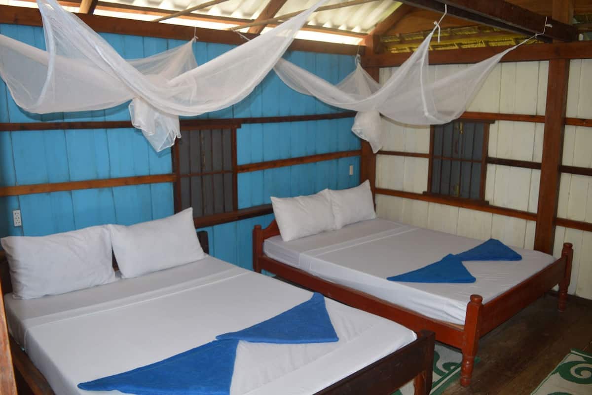 Deux lits simples avec du linge de lit blanc et des serviettes bleues, des têtes de lit en bois et un mur bleu avec une fenêtre.