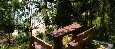 A picnic table set in a forested area with a view of a beach.
