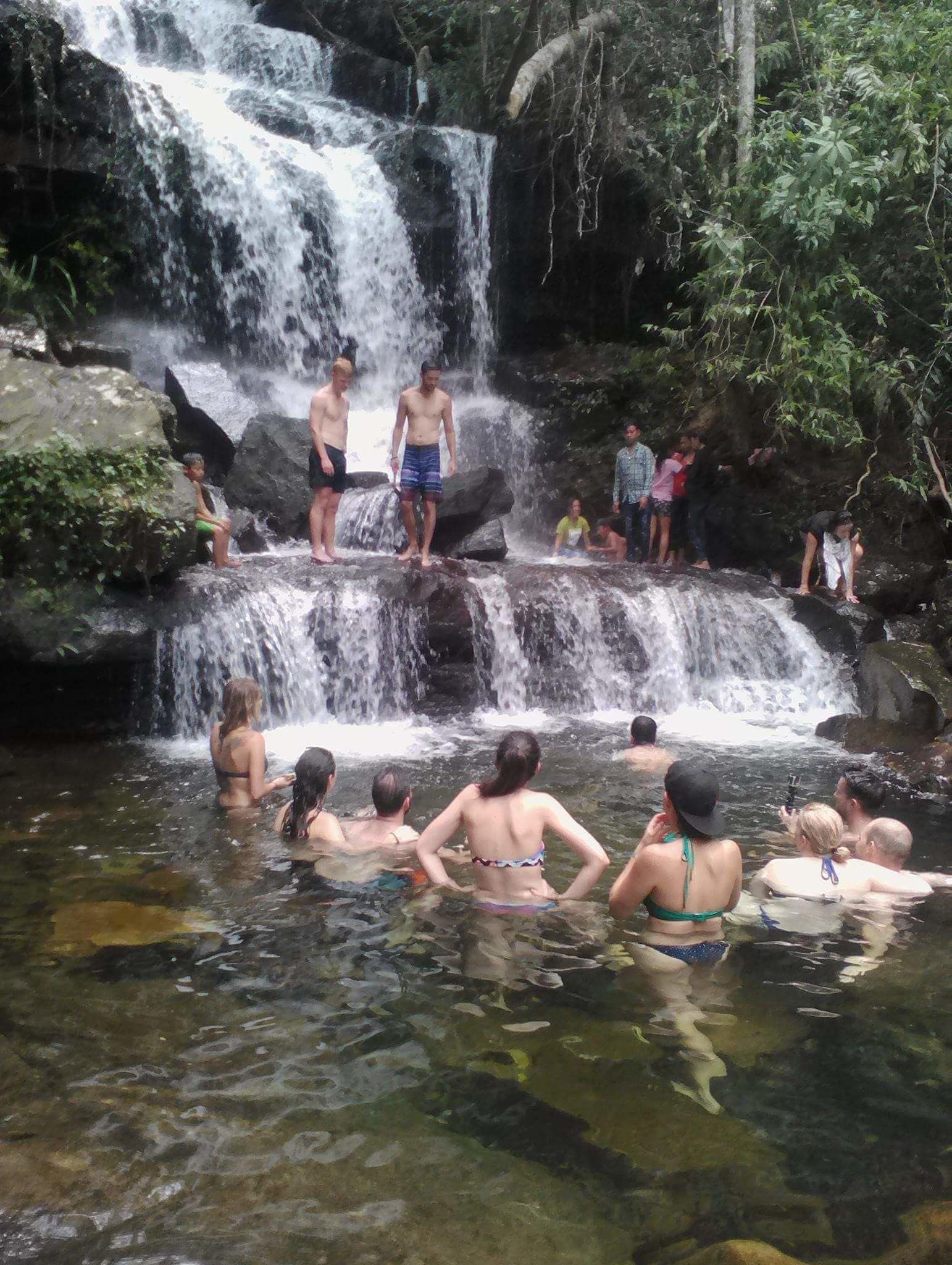 Una cascada con personas sobre rocas y nadando en el agua.
