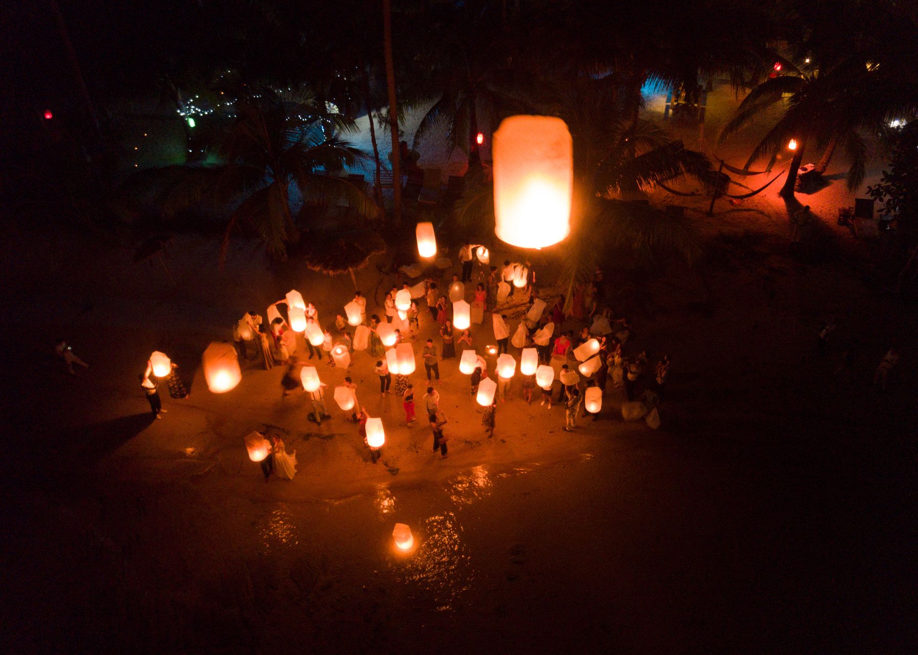 A nighttime outdoor gathering with people holding illuminated lanterns.