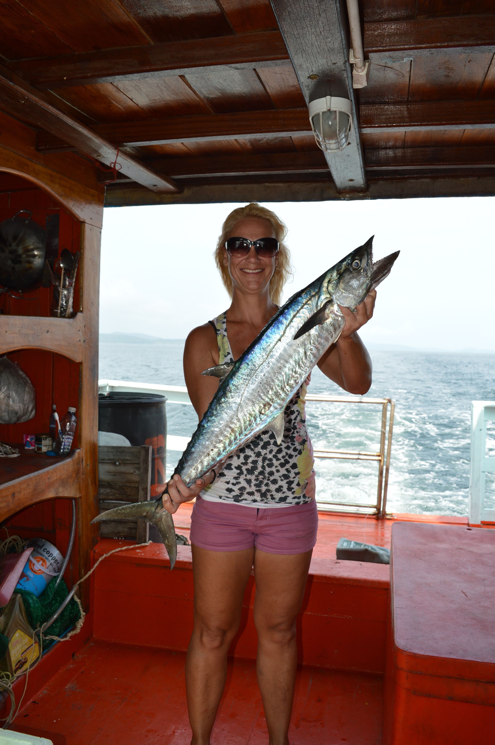 A person holding a large fish on a boat with a wooden interior and a view of the ocean.
