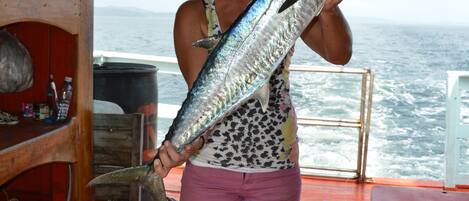 A person holding a large fish on a boat with a wooden interior and a view of the ocean.