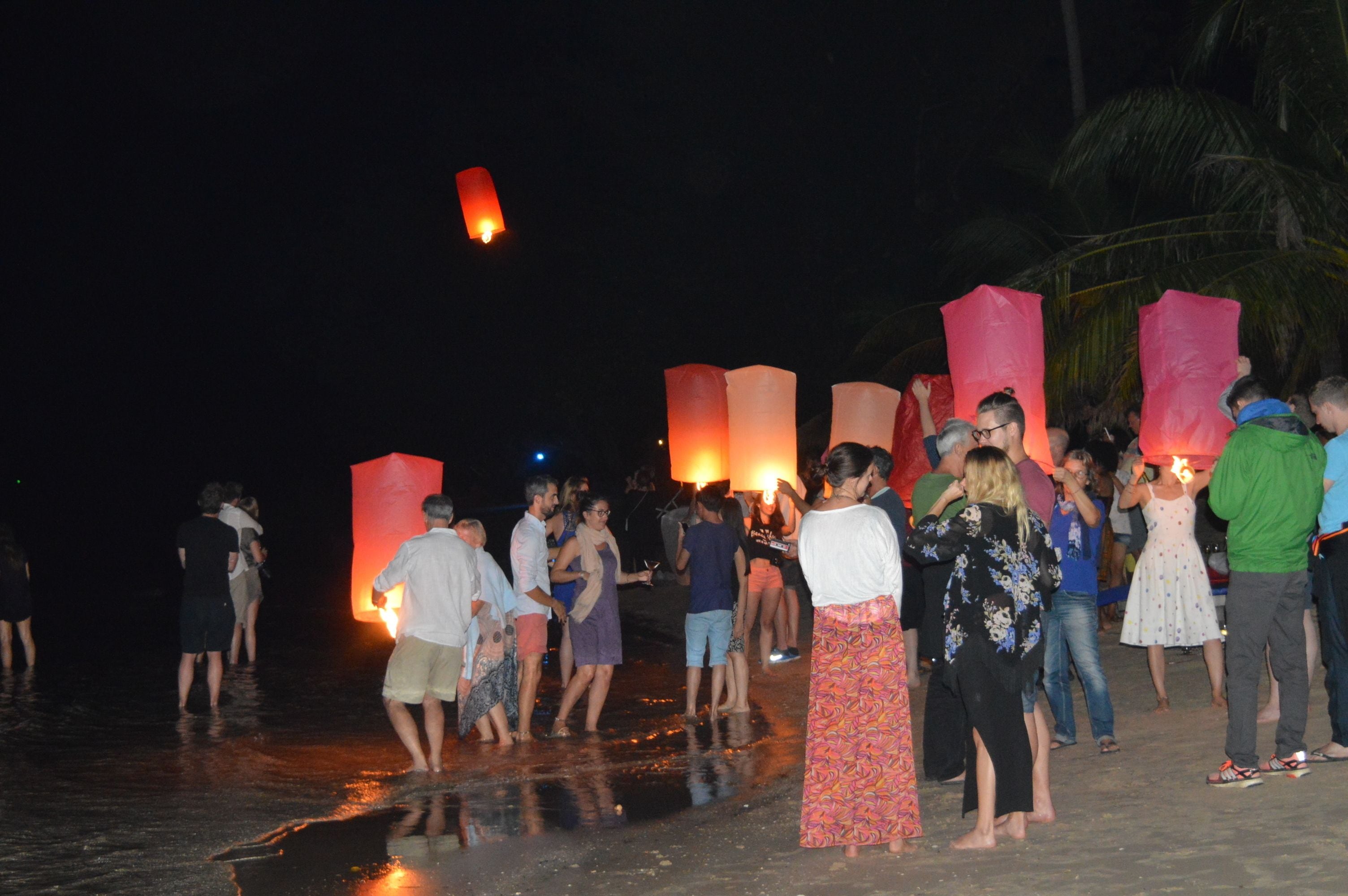 A group of people on a beach at night, some holding lit lanterns.