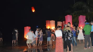 A group of people on a beach at night, some holding lit lanterns.