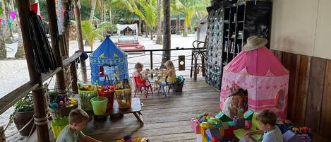 A wooden deck with children playing with toys, a small blue playhouse, and a pink tent.