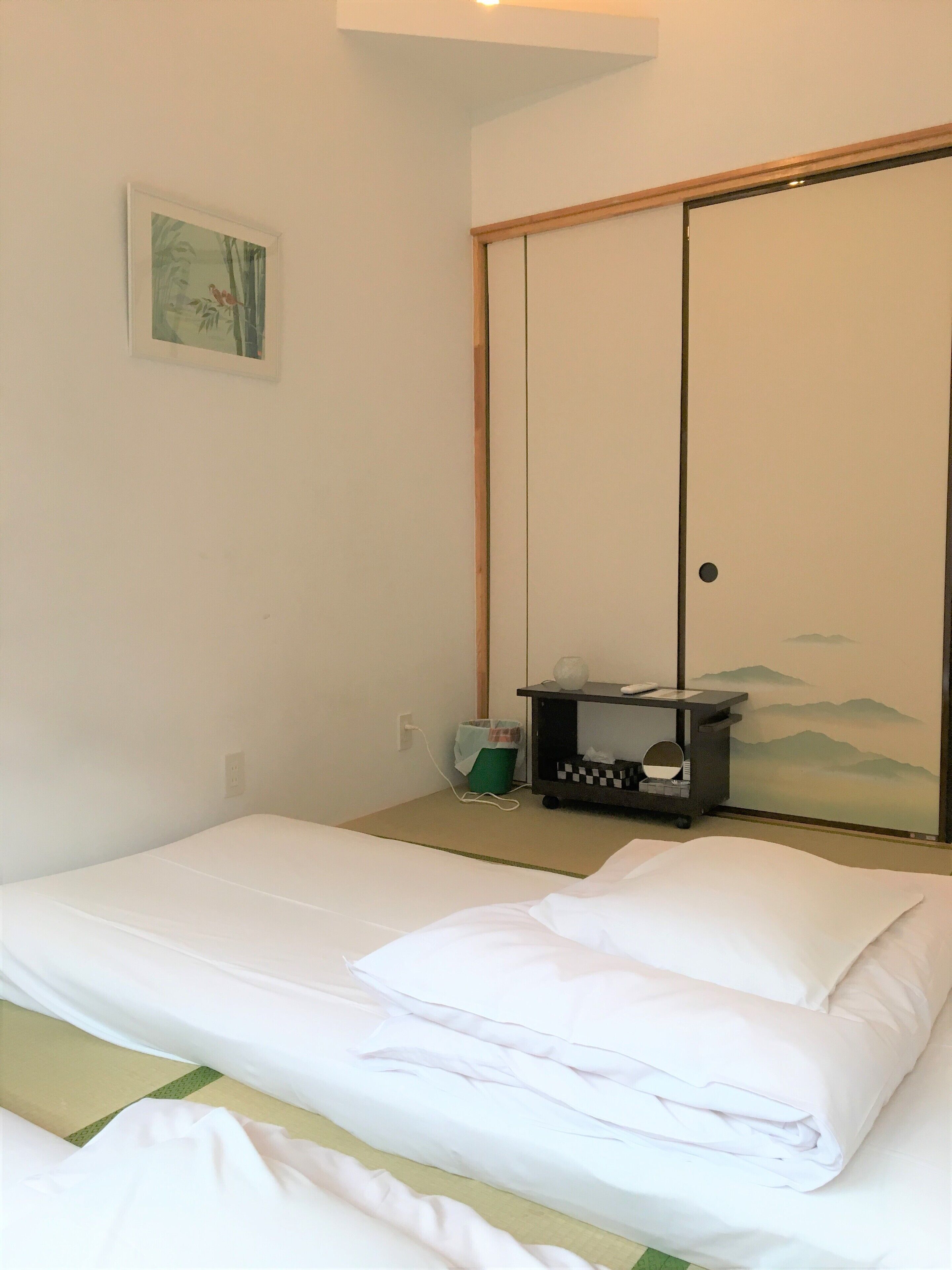 A hotel room with a bed, a small table with a lamp, a trash bin, and a sliding door.