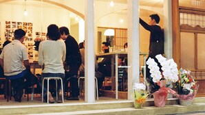 Un restaurante con una decoración moderna, que incluye una barra y una zona de estar. Hay flores expuestas afuera de la entrada.