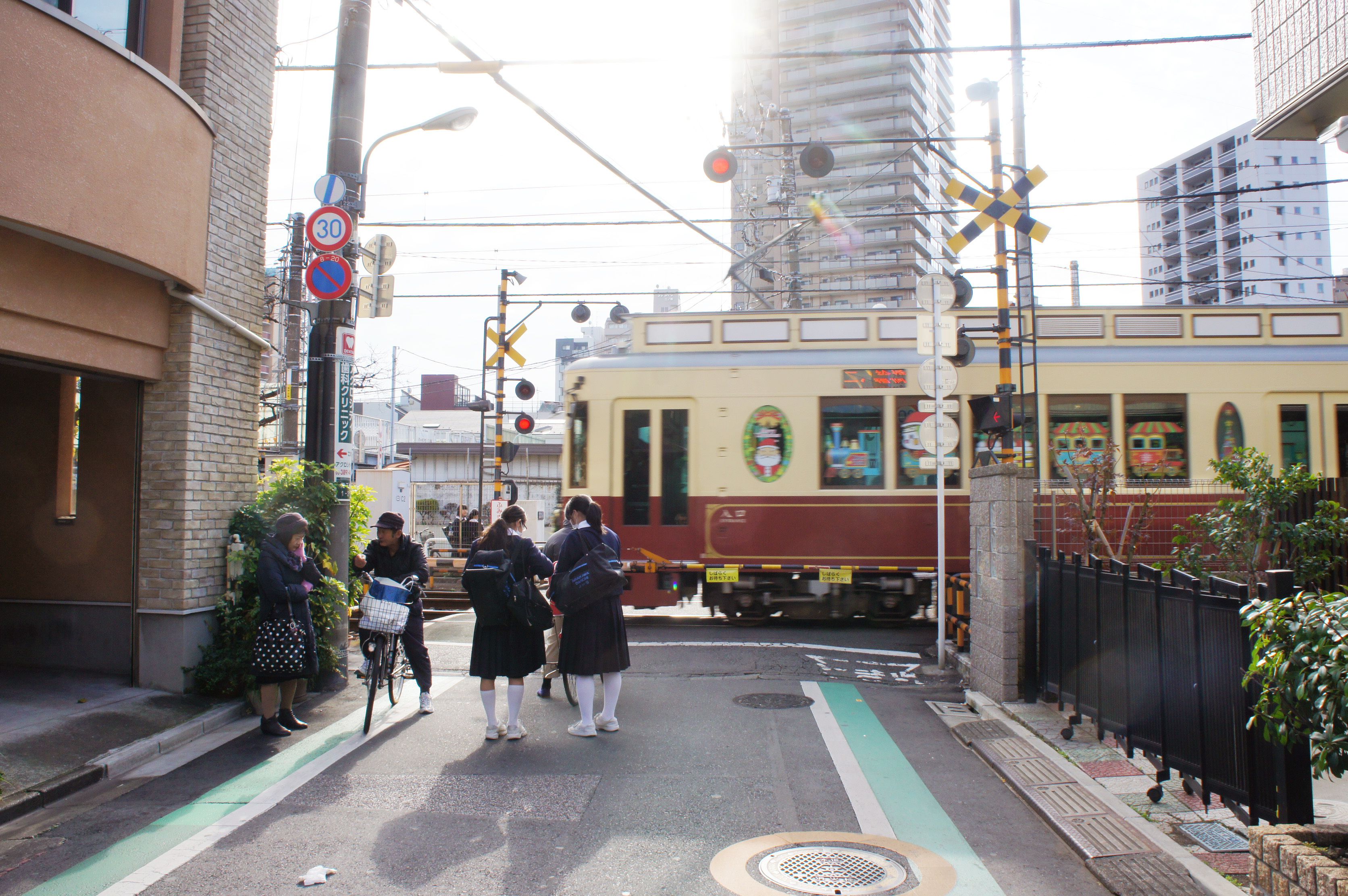 A train crossing with a red and yellow train, a pedestrian crossing, and a building with a brick facade.