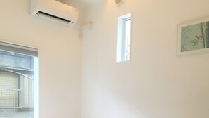 Una habitación con dos camas, una ventana, aire acondicionado y un pequeño cuadro en la pared.
