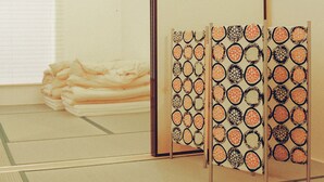 Una habitación con esteras de tatami, una mesa baja con un montón de esteras dobladas y un panel decorativo con diseños circulares.