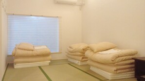 Una habitación pequeña y limpia con una cama, una ventana con persianas, aire acondicionado instalado en la pared y suelo de estera de tatami.