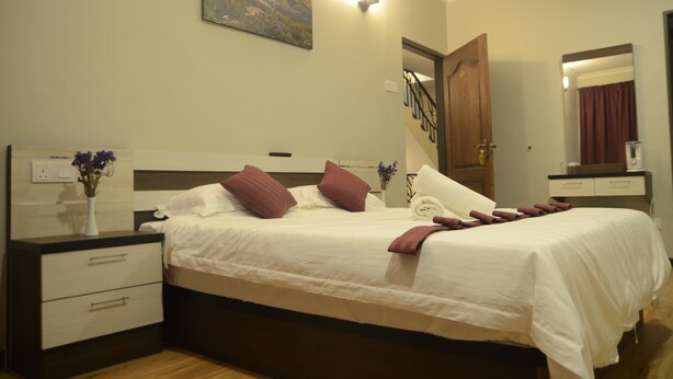 A neatly made bed with white and brown bedding, a bedside table with a vase of flowers, and a painting on the wall. - Zermatt Hotel (Tanah Rata)