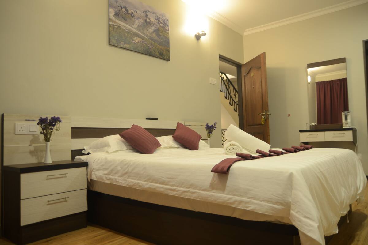 A neatly made bed with white and brown bedding, a bedside table with a vase of flowers, and a painting on the wall.