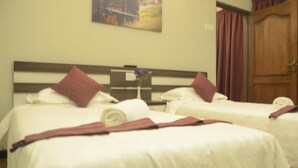 A hotel room with two beds, each with white bedding and red pillows. There is a wooden headboard, a painting on the wall, and a door with curtains. - Zermatt Hotel (Tanah Rata)