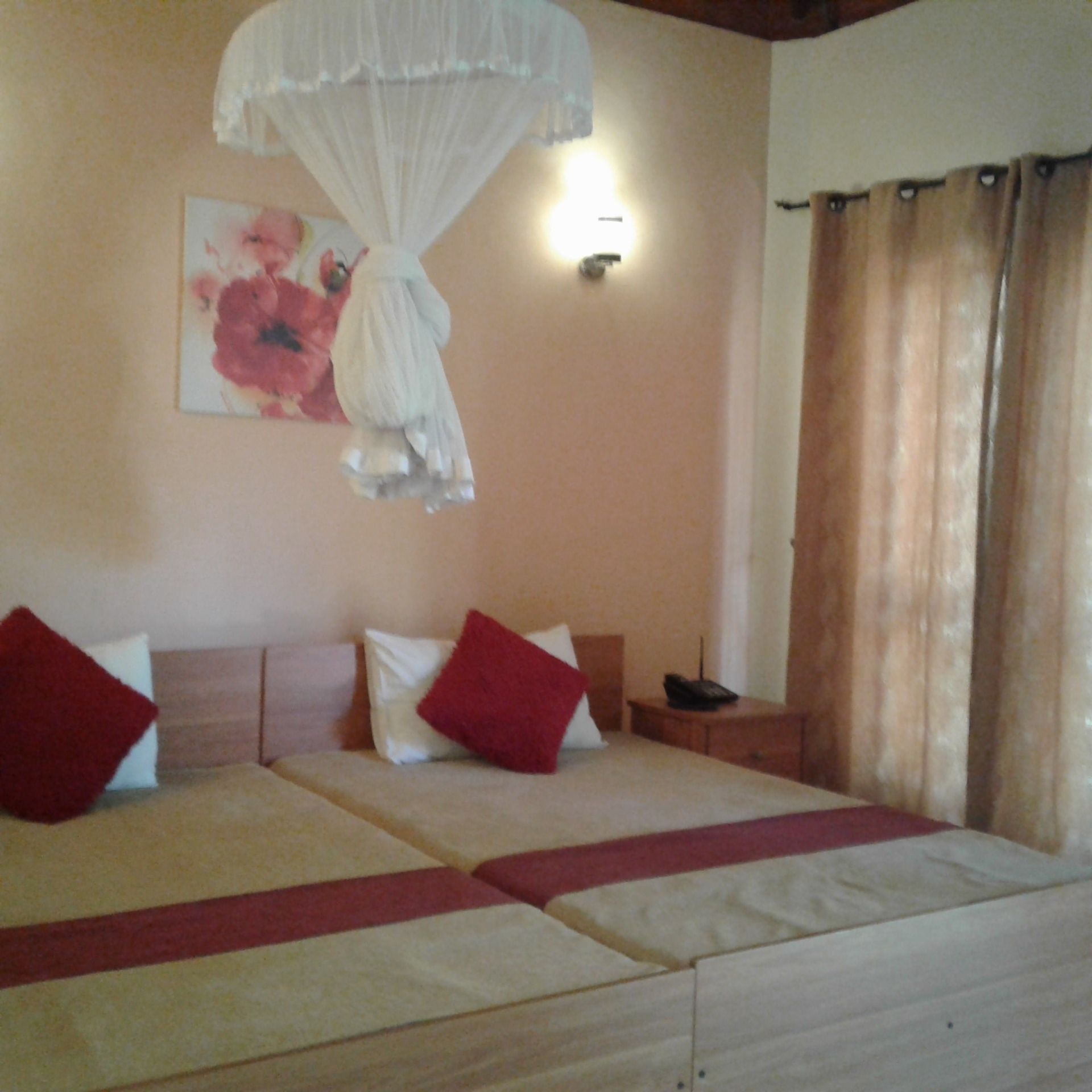 A hotel room with two beds, a bedside table, a lamp, and a curtain.