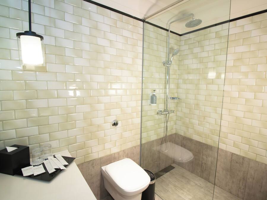 Un baño moderno con ducha acristalada, paredes de azulejos blancos y un inodoro blanco.