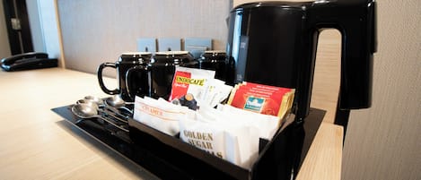 A coffee station with a coffee maker, cups, and sugar packets.