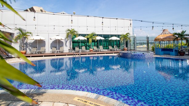 Ein Swimmingpool mit Liegestühlen und Sonnenschirmen, ein Glasgebäude und ein Gebäude mit einem Reetdach.