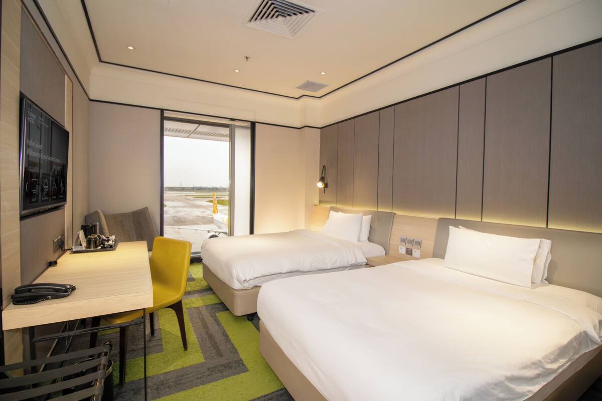 Een hotelkamer met twee bedden, een bureau, een stoel en uitzicht op het omliggende landschap.