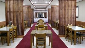 A restaurant with a central dining area featuring tables and chairs arranged in rows, flanked by wooden paneling. - Ra Hotel (Jeju City)