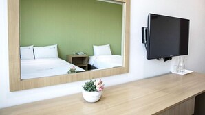 A hotel room with a bed, bedside table, mirror, TV, and a small potted plant. - Ra Hotel (Jeju City)