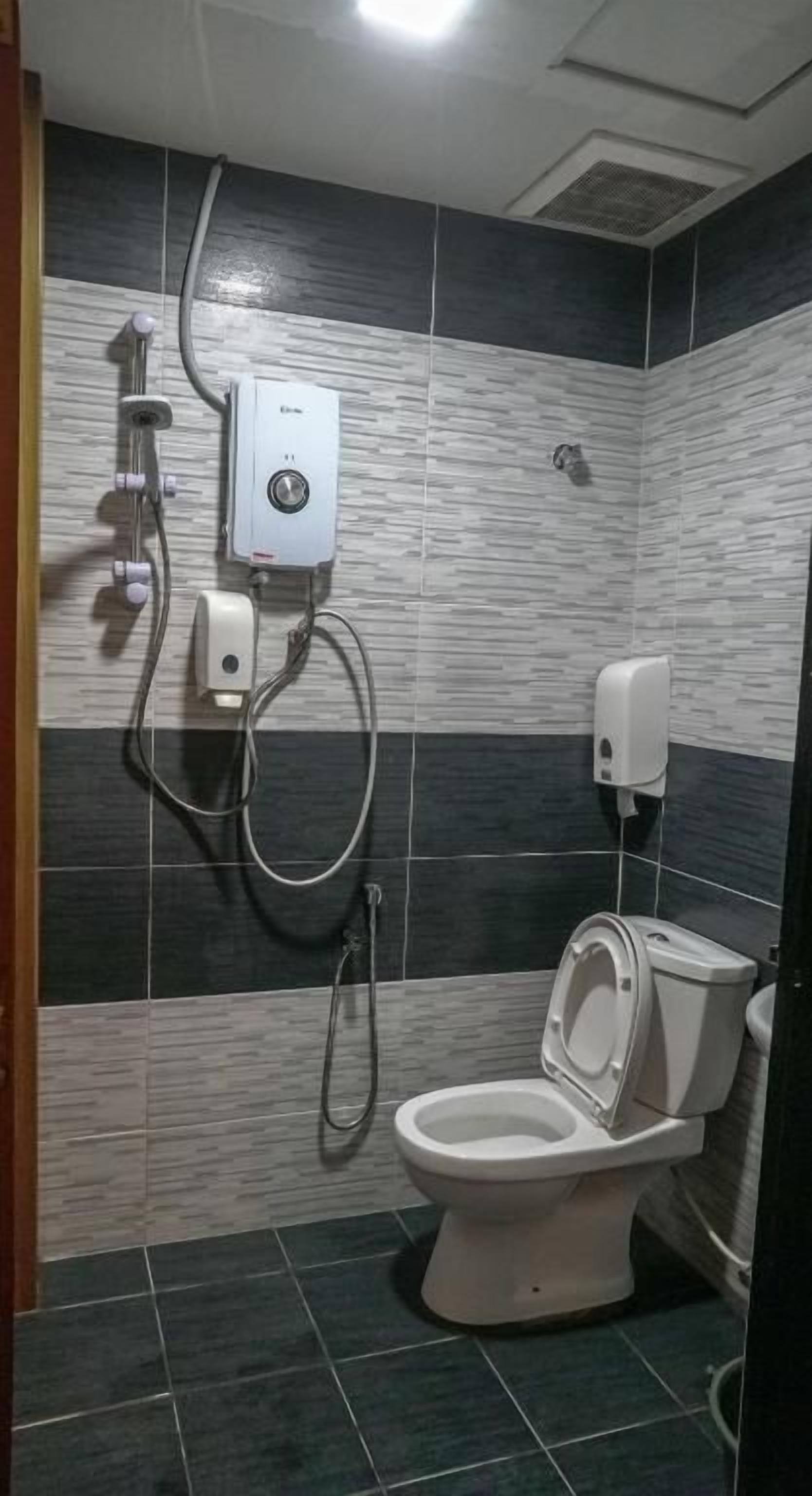 A bathroom with a toilet, a shower unit, and a soap dispenser.