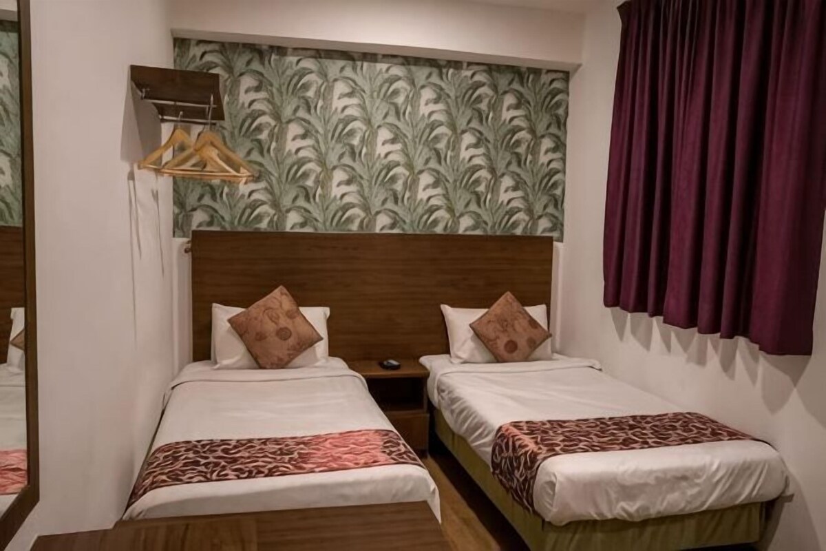 A hotel room with two beds, a wooden headboard, a hanging coat rack, and a patterned wallpaper.