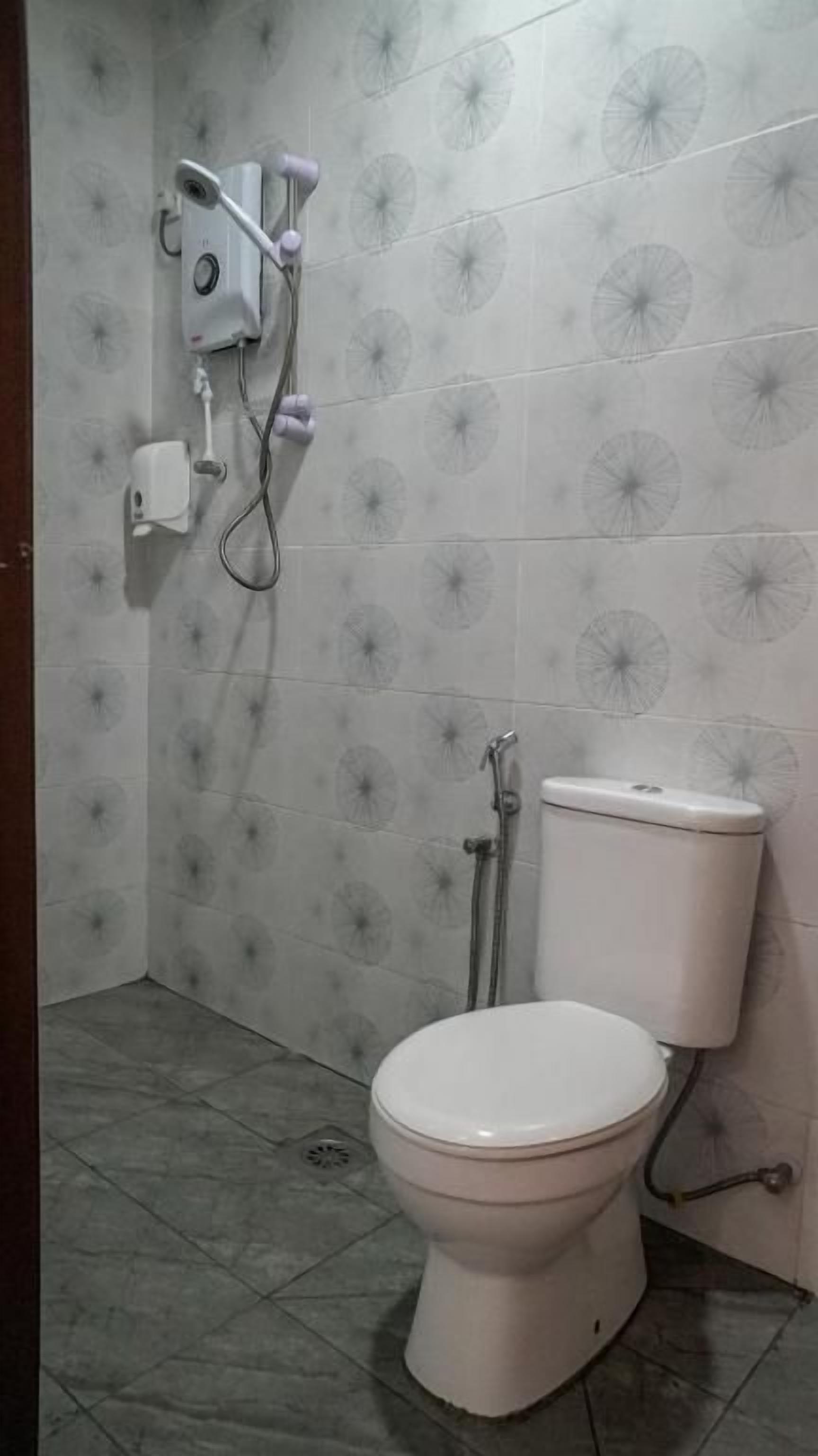 A bathroom with a toilet, a shower unit, and patterned tiles.