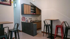 A compact kitchen with a built-in island, a sink, and a small countertop. There are two stools and a table with chairs. - Highlanders Hotel (Tanah Rata)
