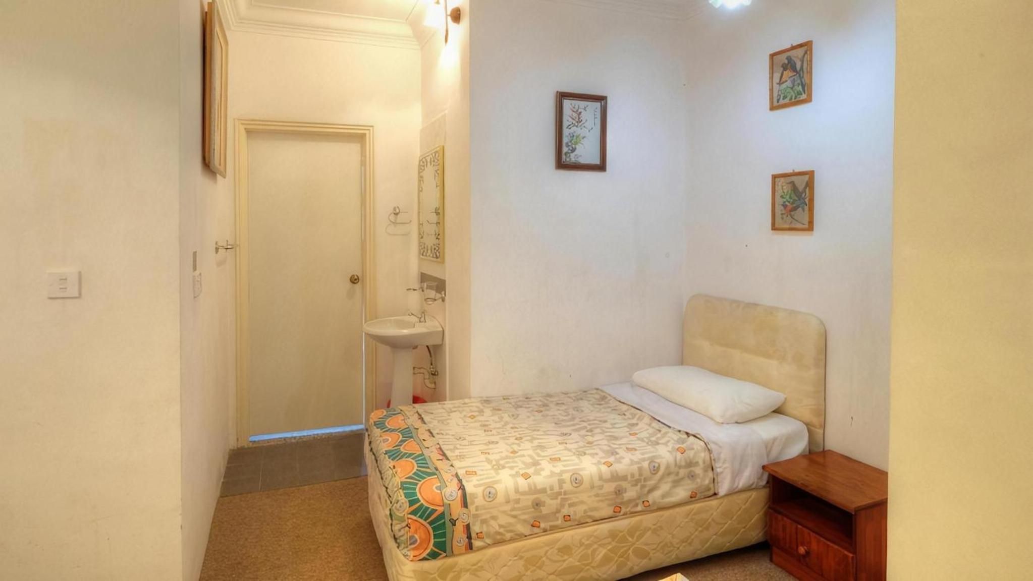 Un dormitorio con cama, mesita de noche, un pequeño armario y estante en la pared.