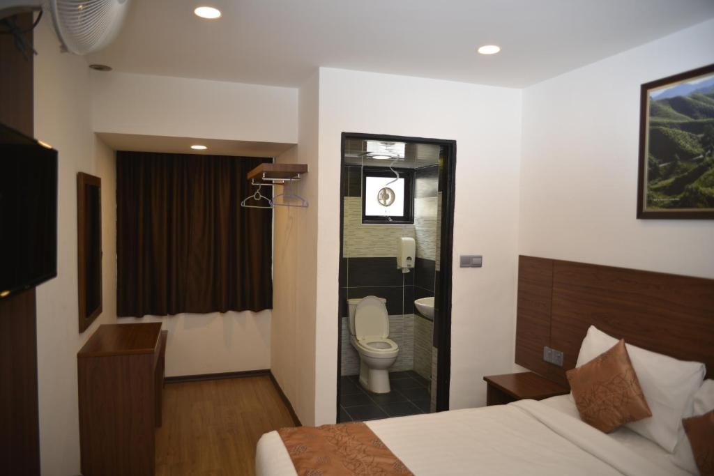Une chambre d’hôtel avec un lit, une table de chevet, une télévision, un miroir et une salle de bain visible à travers une porte ouverte.