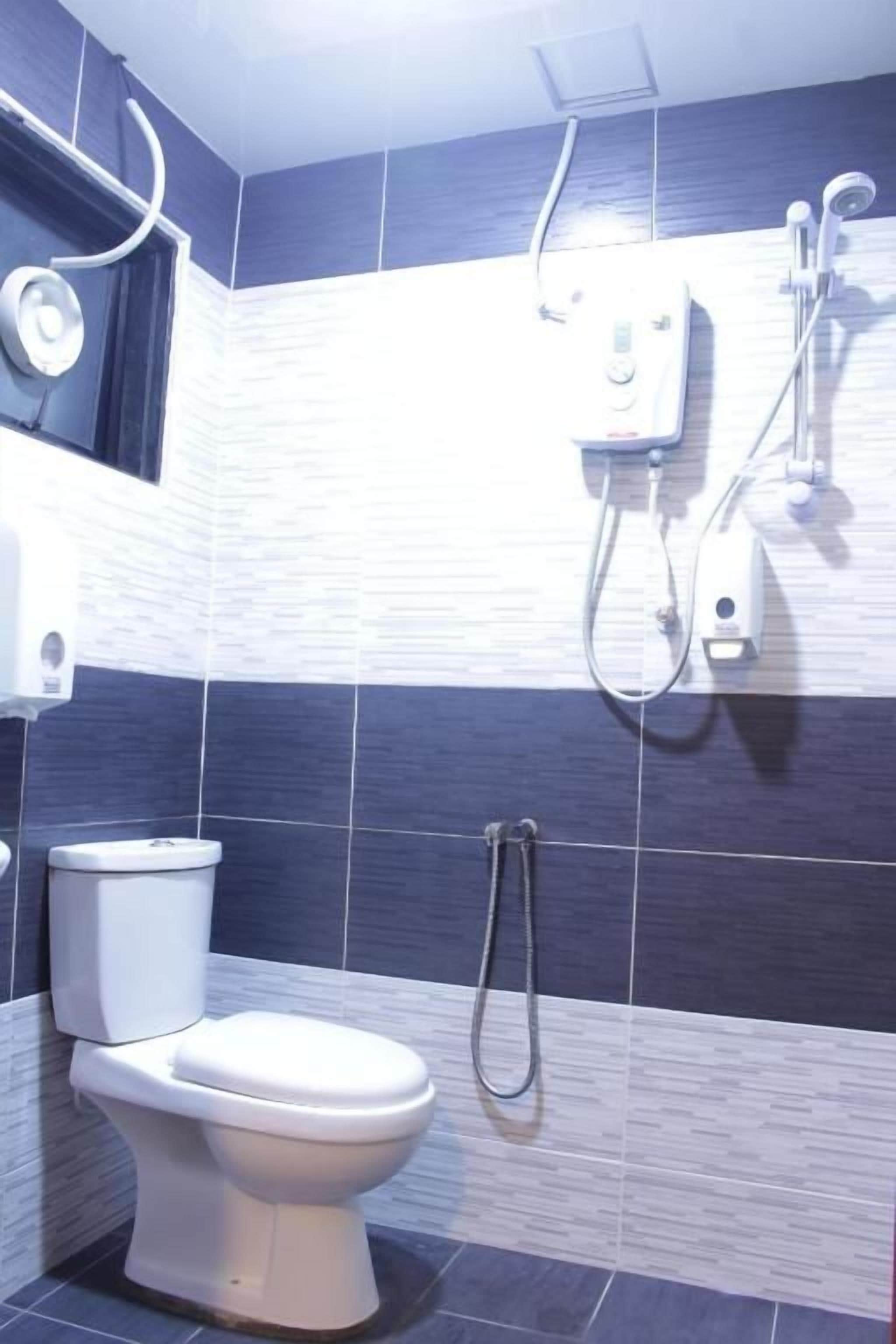 Casa de banho com sanita, chuveiro e torneira fixada na parede.
