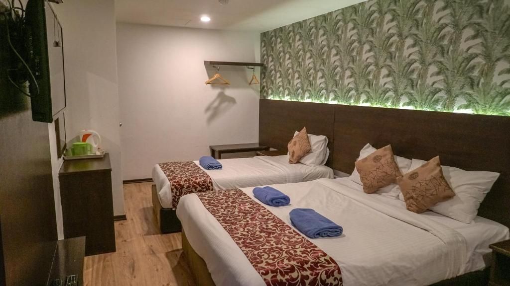Una habitación de hotel con dos camas, una mesita de noche, un televisor y un estante en la pared.