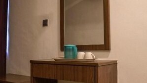Un escritorio de madera con un espejo, un cesto de basura y una taza azul.