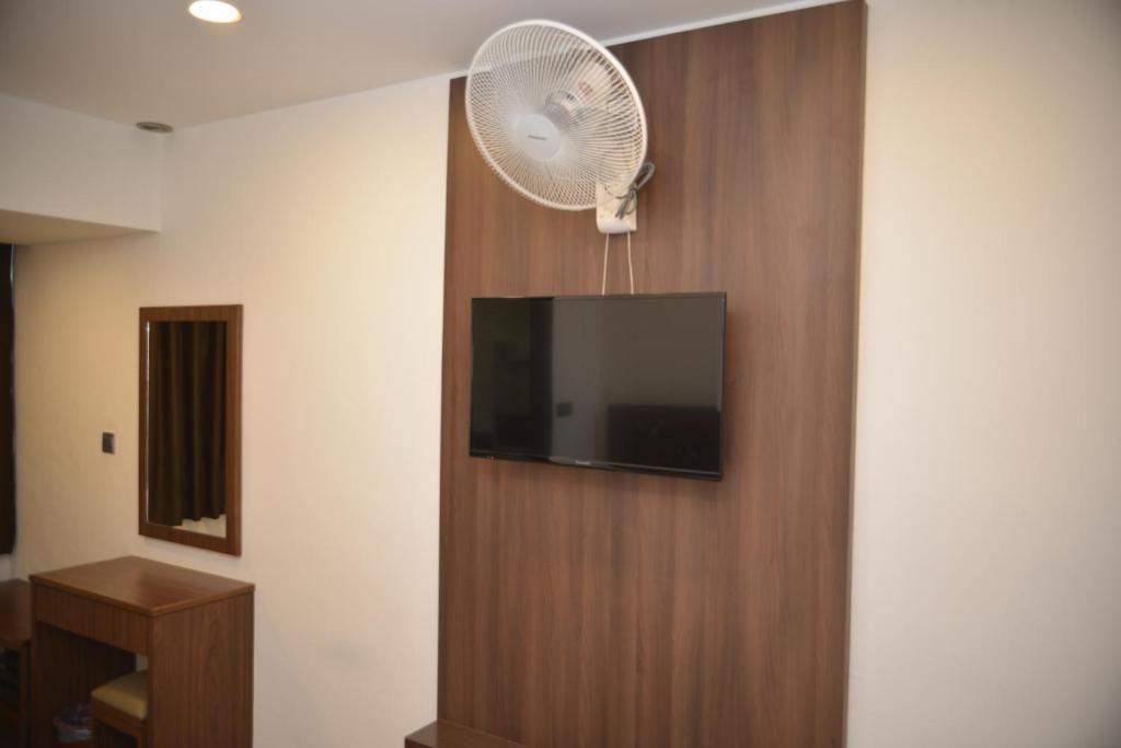 A room with a mounted flat-screen TV, a standing fan, and a wooden cabinet.