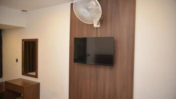 A room with a mounted flat-screen TV, a standing fan, and a wooden cabinet.