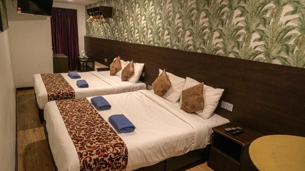 A hotel room with two beds, each with a patterned bedspread, pillows, and a remote control on a side table.