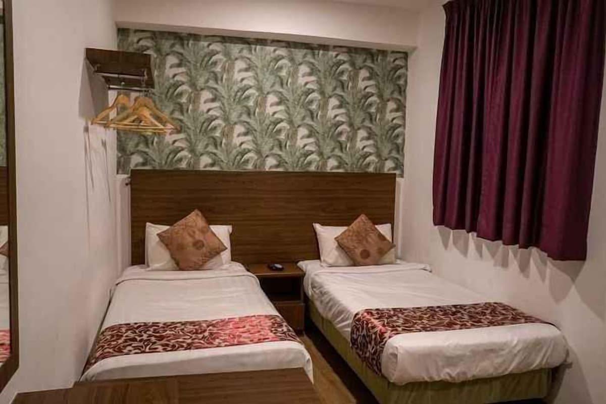 A hotel room with two single beds, a wooden headboard, a mirror, and a patterned wallpaper.