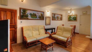 Una sala de estar con un conjunto de sofá, una mesa de centro y dos sillas. Hay cuadros en las paredes y una puerta a la izquierda.